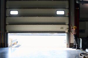 Young female worker of factory or hangar opening shutter roller door